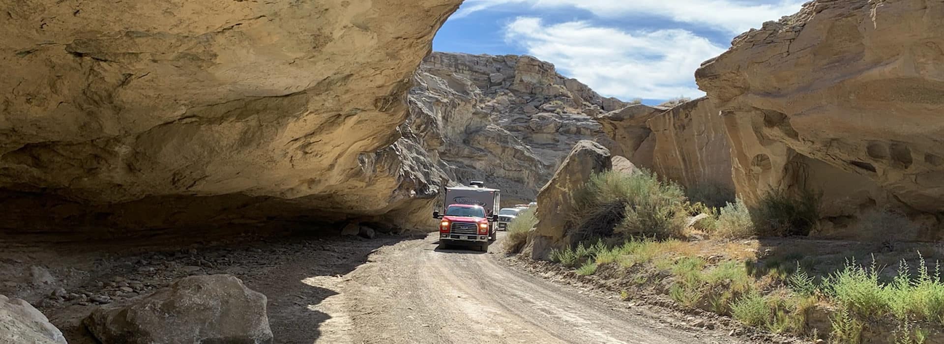 Truck and camper driving on Crosby Canyon Road under low hanging outcropping