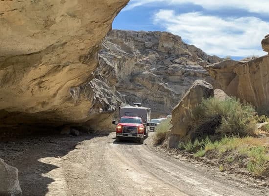 Truck and camper driving on Crosby Canyon Road under low hanging outcropping