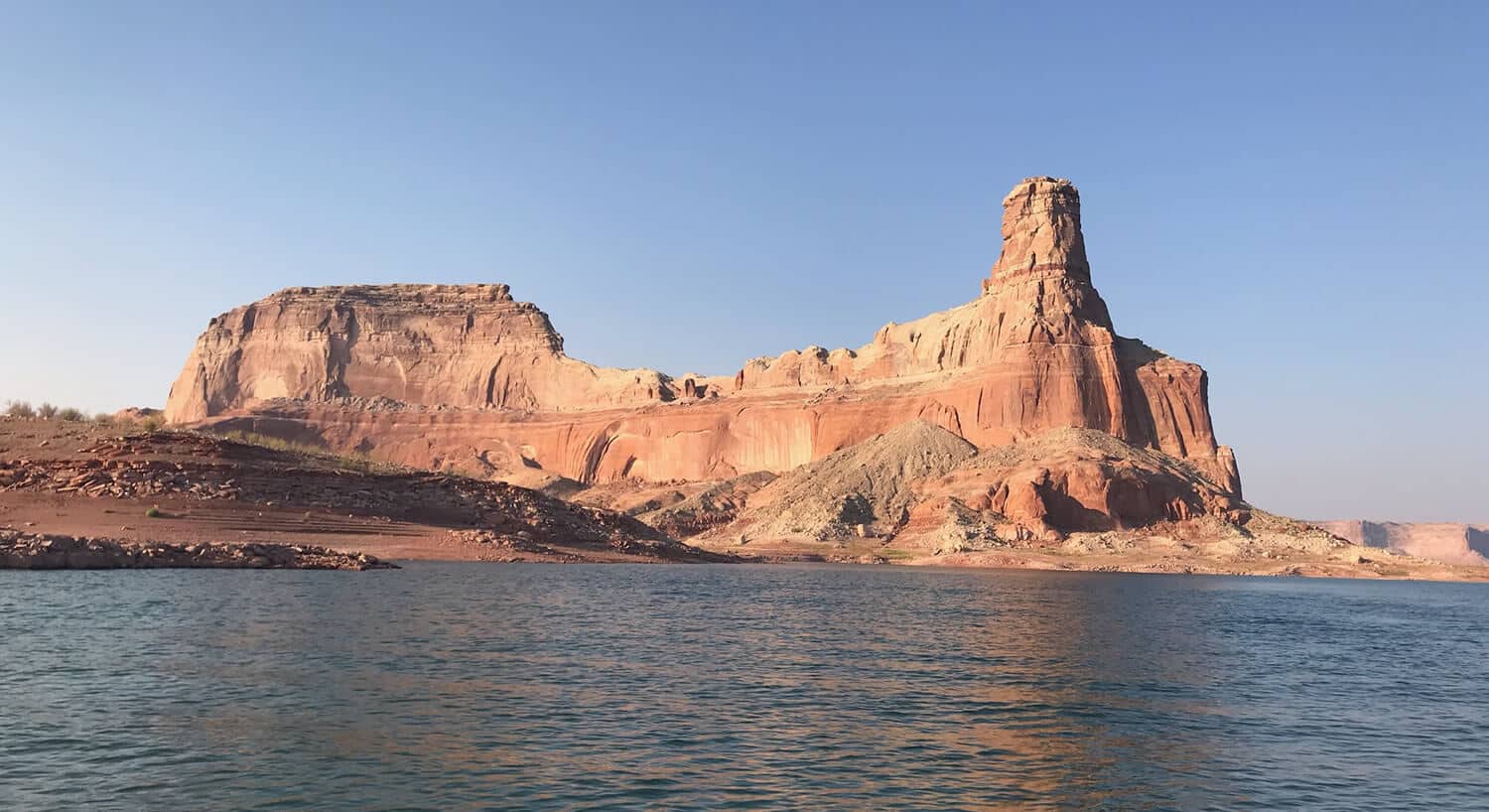 View across rippling water toward red and tan rock formations with jagged edges.