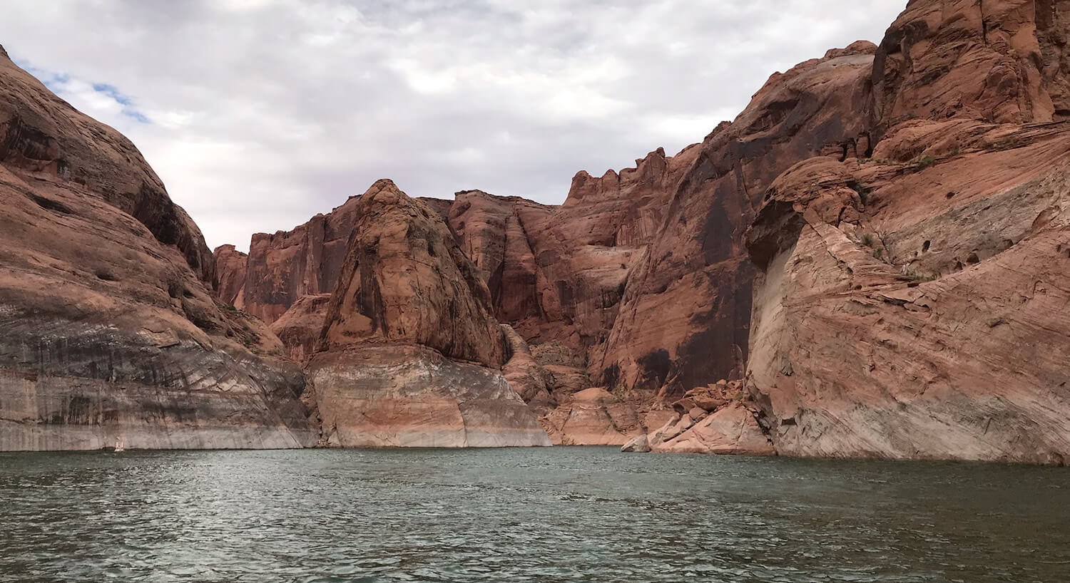 Red rock formations with water markings surrounding peaceful cove.