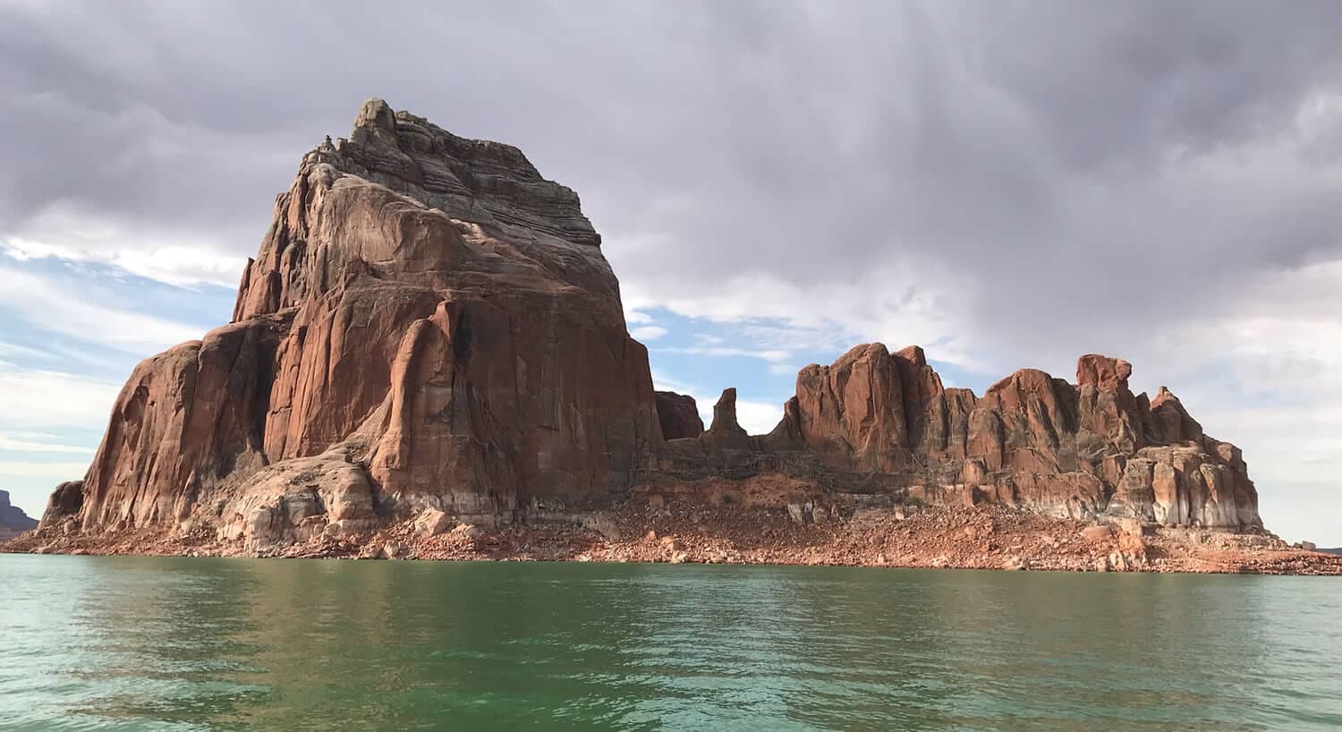 View across water toward pointed cathedral looking red rocks under cloudy sky