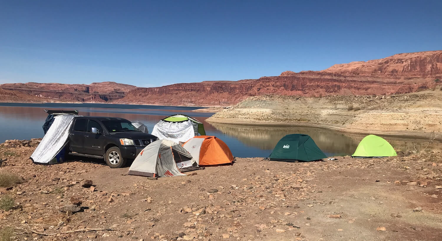 Grey Titan truck with cab on beach setup with various colored tents and red rocks in the distance