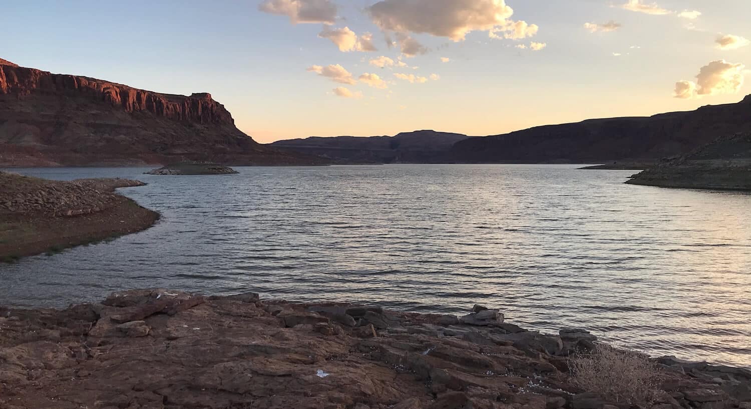 View from beach of peaceful cove with rippling water surrounded by red rock formations on all sides.