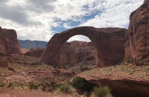 red rock formations all around with view through an arch with additional formations in distance, blue skies with fluffy white clouds overhead.